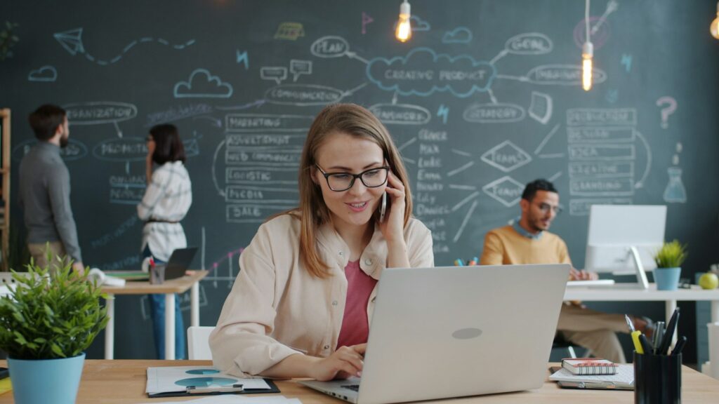 A woman answering a phone call from a new lead while working on her laptop