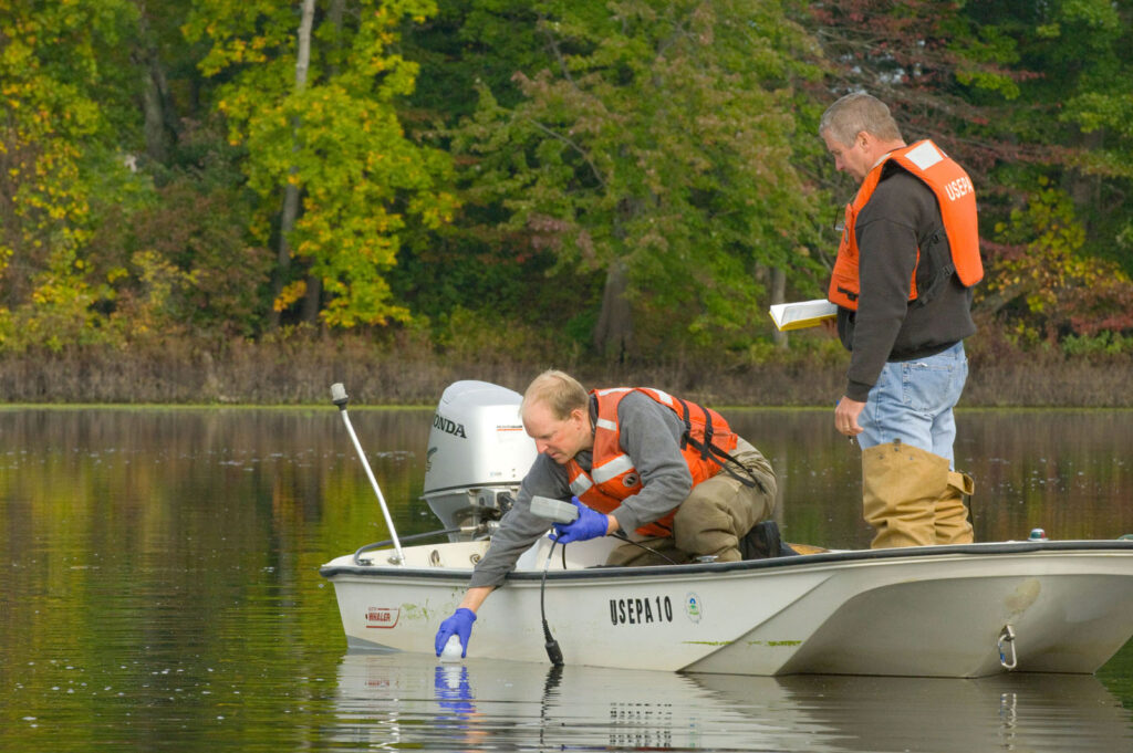 Two scientists in life vests collecting water samples from a small boat on a lake