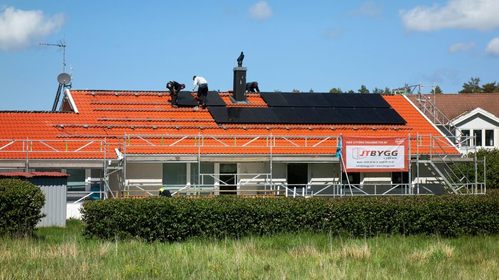 Three installers fitting black solar panels on an orange tiled roof